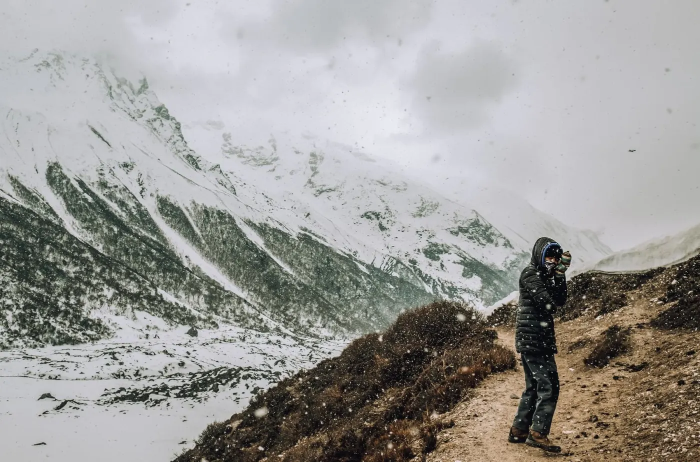 A trekker photographing snowy mountains from a rocky trail
